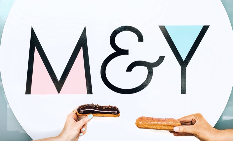 A chocolate éclair and a croissant held up in front of the Madame & Yves sign