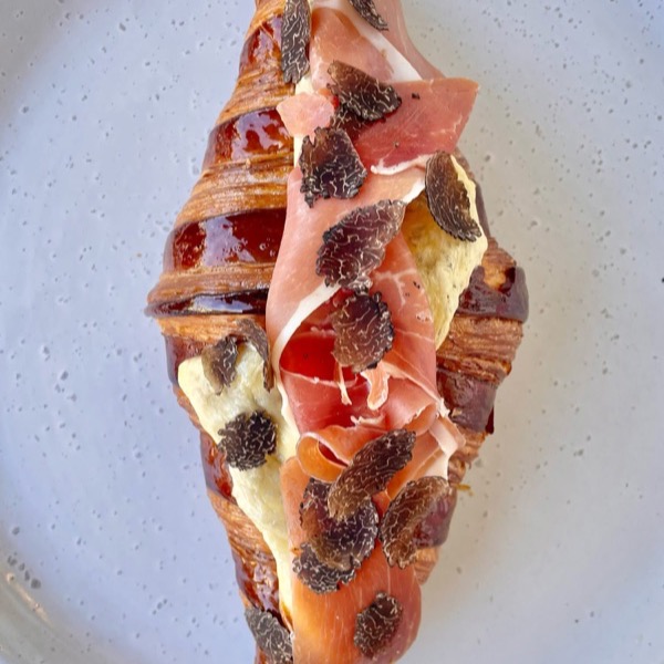 A truffle and prosciutto croissant on a speckled plate
